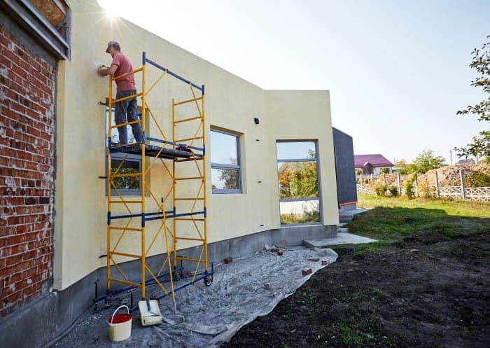 Person beim Arbeiten an einer Fassade auf einem zuvor aufgebautem Arbeitsgerüst.